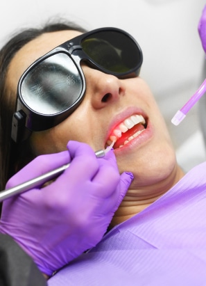 Dental patient with black-eye-protection-glasses on getting laser treatment by a dentist wearing purple latex gloves.