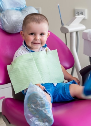 Young child sitting in dentist chair with dental bib.