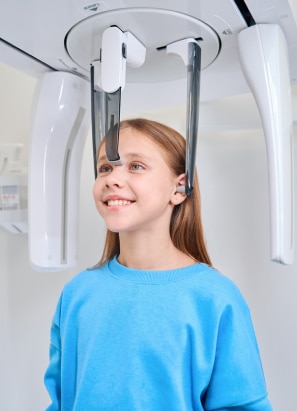 Girl in blue shirt standing in dental x-ray scanner.