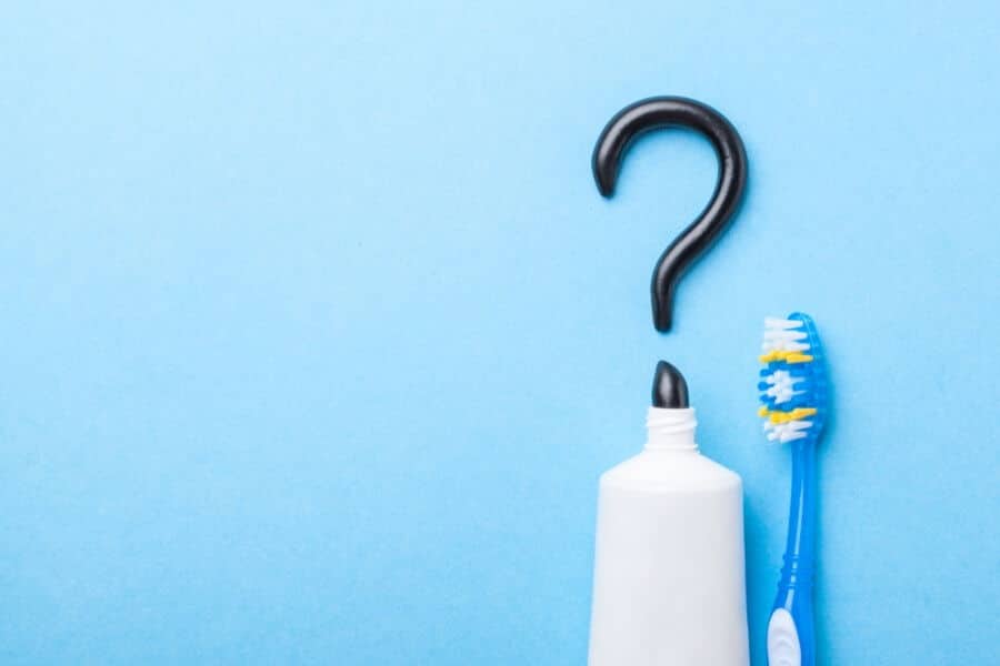 A toothbrush and toothpaste on a blue background, with black toothpaste forming a question mark above the open tube.