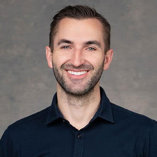 Headshot of Dr. Justin Stevens wearing a dark-colored button-down-collared-shirt against a gray photography backdrop.