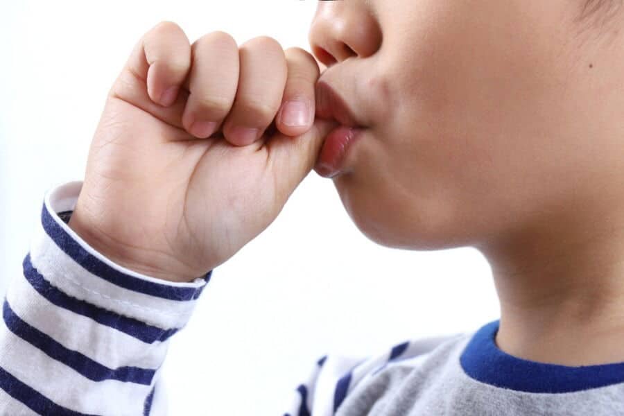 Child in striped shirt sucking thumb, side profile, against a plain background. Facial expression is calm and thoughtful.