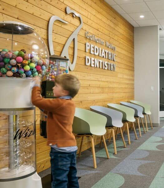 A dental office lobby with colorful toys, seating, and two children. Sign reads "Pediatric Dentistry." Bright, playful decor enhances the welcoming atmosphere.